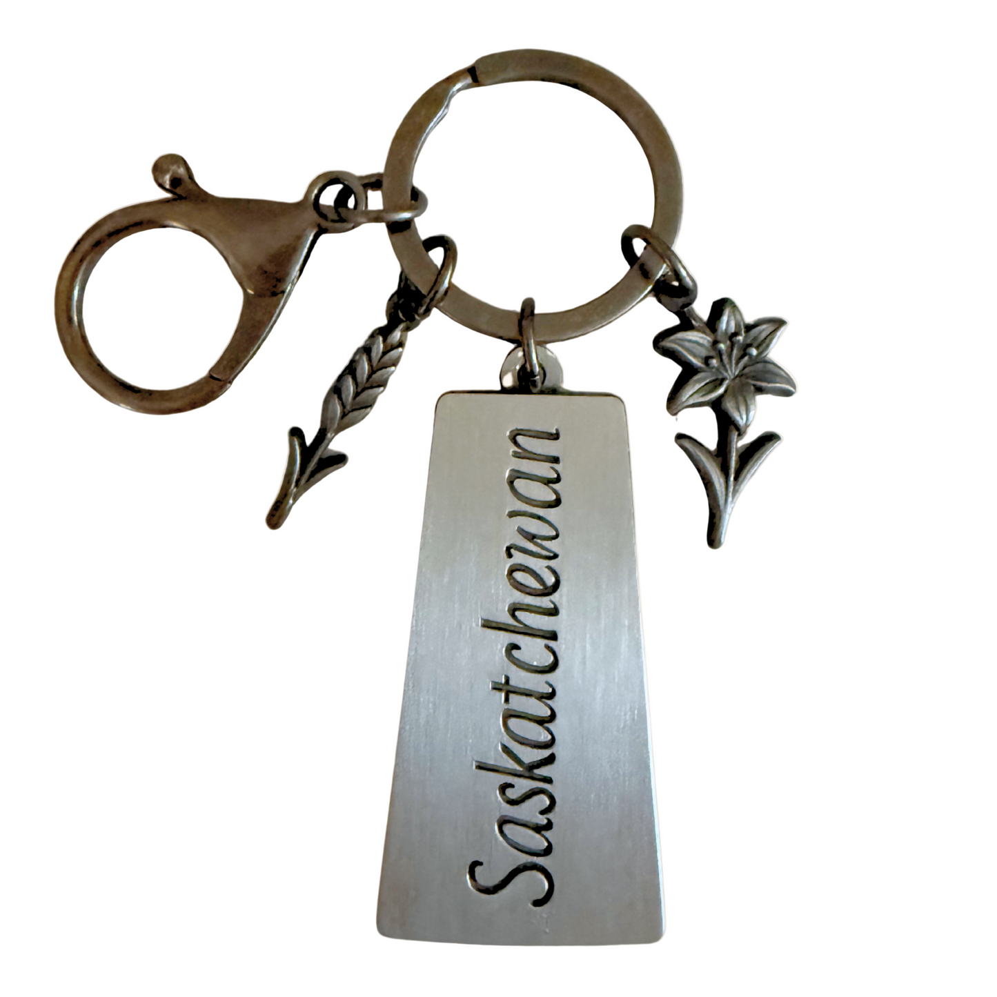 Metal keychain with a Saskatchewan-shaped engraved tag, wheat stalk charm, and Prairie Lily charm on a keyring with lobster clasp.