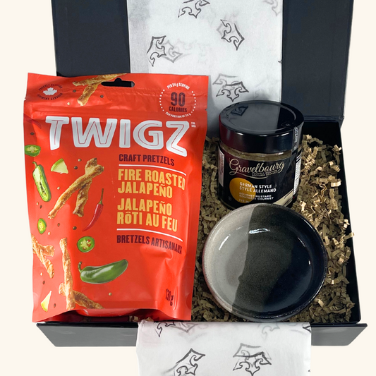 A beautifully packaged gourmet gift box featuring fire-roasted jalapeño pretzel sticks, Gravelbourg mustard, and a handcrafted ceramic dipping bowl by Freba Pottery.