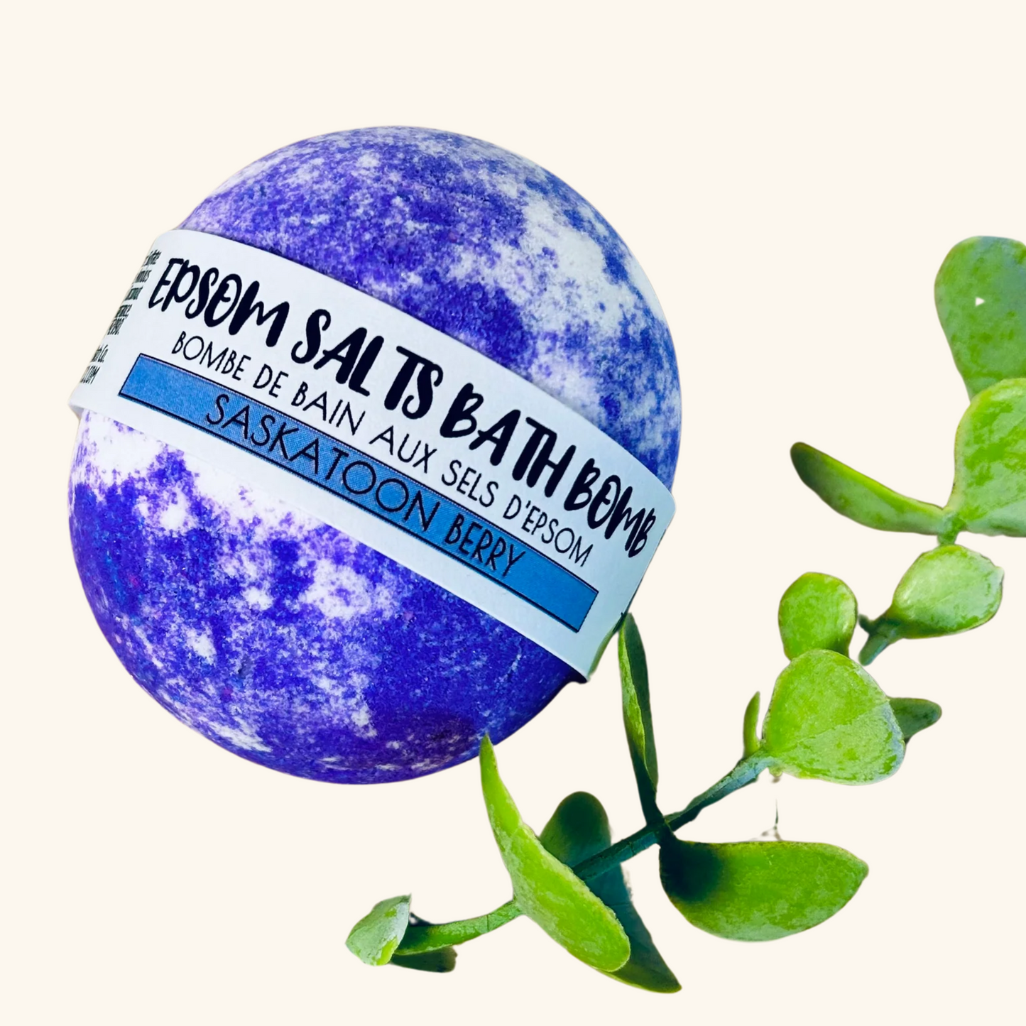 urple and white marbled Epsom salts bath bomb labeled Saskatoon Berry by The Sask Bath Co., surrounded by fresh eucalyptus.