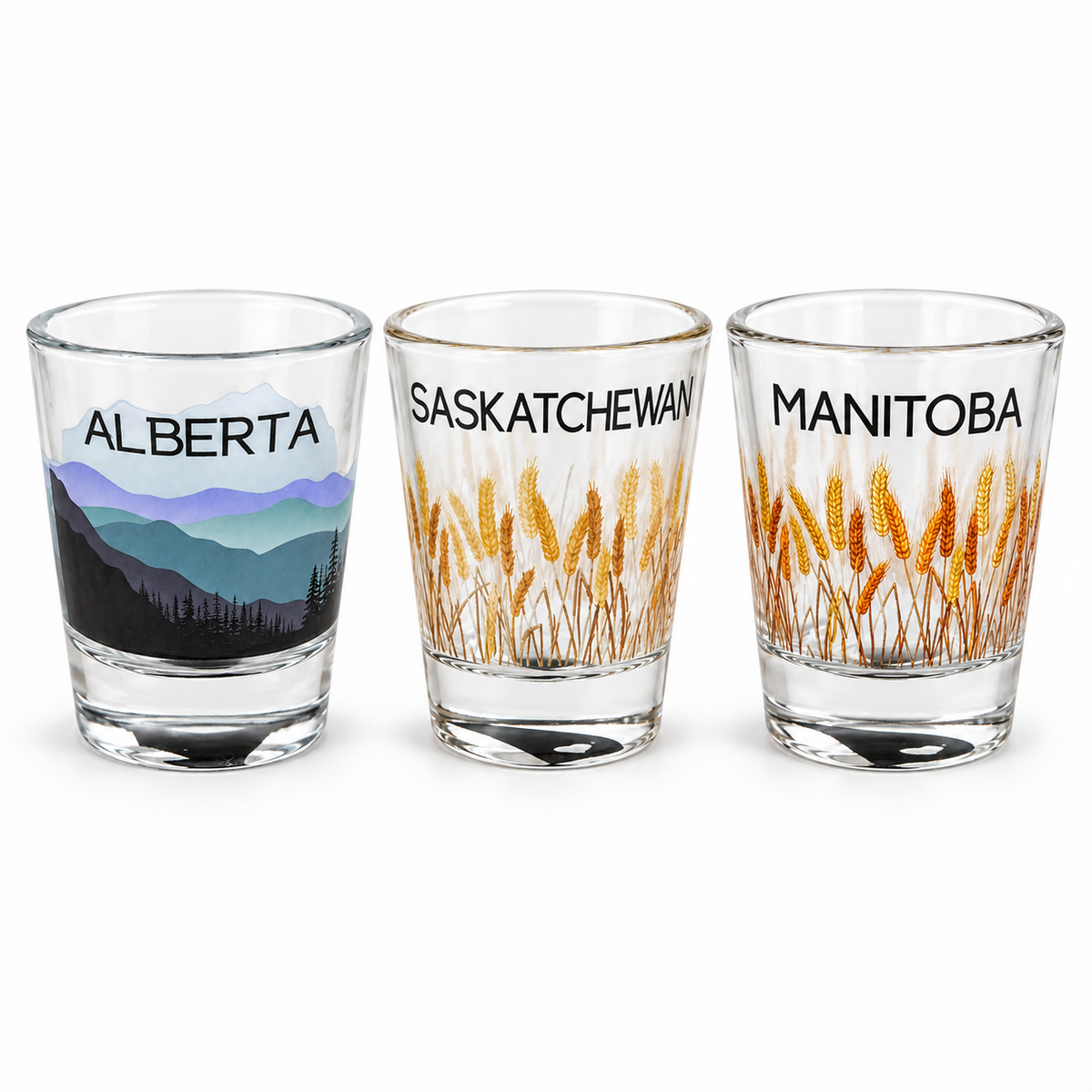 Alberta, Saskatchewan and Manitoba 1 oz shot glasses with mountain and golden wheat designs, displayed together on white.