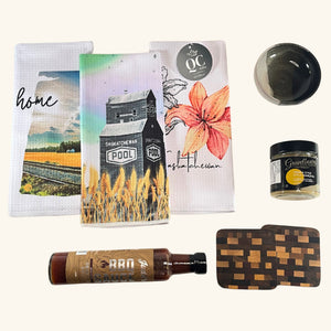 A selection of artisan kitchen essentials, including a handcrafted Freba Pottery dish, Gravelbourg Mustard, Judd’s BBQ Sauce, wooden coasters, and Prairie-themed tea towels.