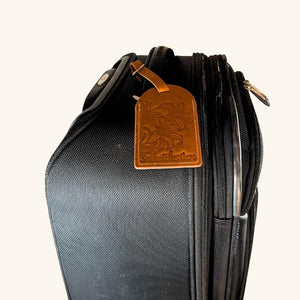 Prairie Lily leather luggage tag securely fastened to a suitcase, providing a stylish and identifiable travel accessory