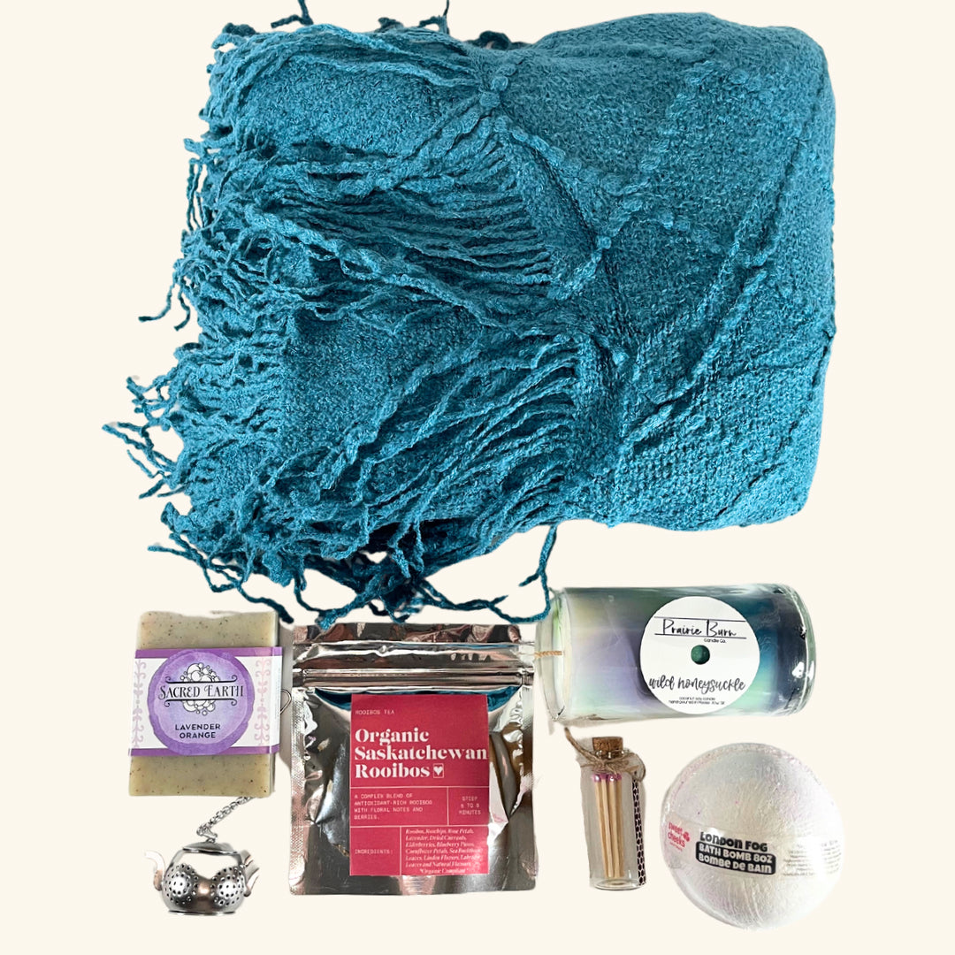 A collection of handcrafted Prairie-made wellness products, including tea, bath essentials, a soy candle, and a cozy blanket.