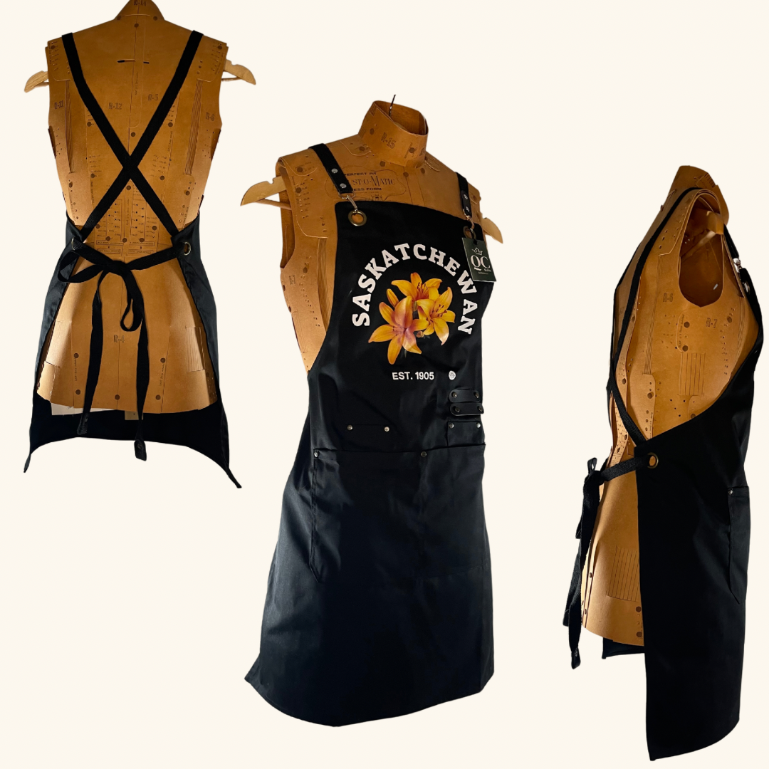 Black apron featuring Saskatchewan's outline and hand-pressed Prairie Lily design, a stylish and functional piece for any cook or crafter